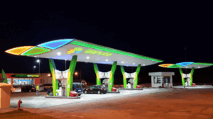 Station-service moderne avec auvents lumineux et design coloré, équipée de plusieurs pompes et d’un espace boutique.