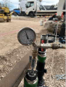 Manomètre et raccords utilisés pour un test de pression et d’étanchéité sur chantier, avec équipements de contrôle visibles.